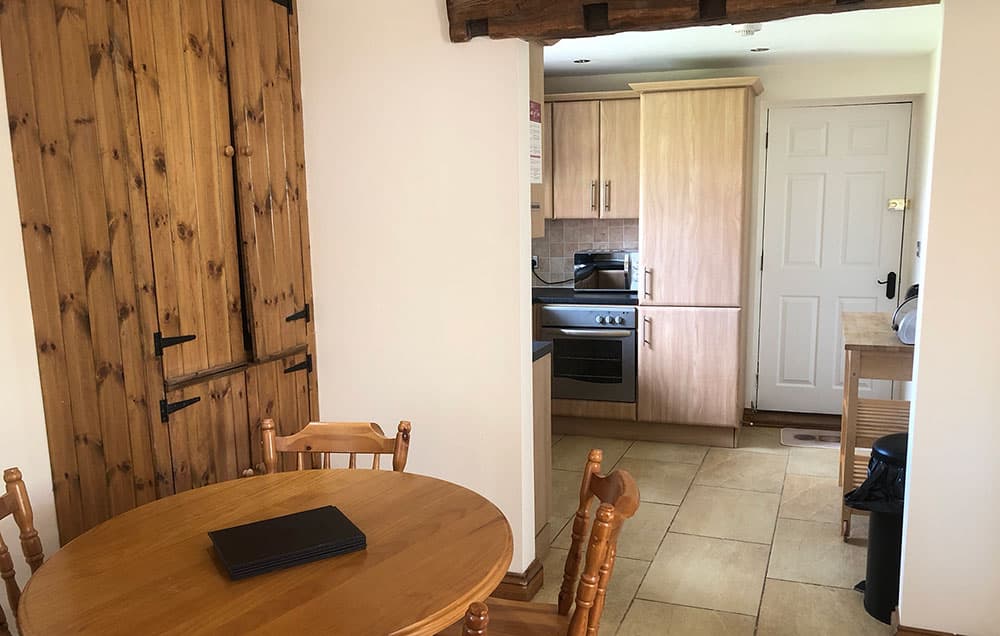 Round dining table and chairs beside a wooden stable door, with the kitchen and back door beyond