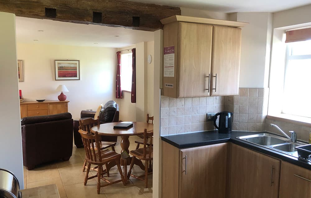 Kitchen with oak units and a black worktop, looking through to a round dining table and leather sofas