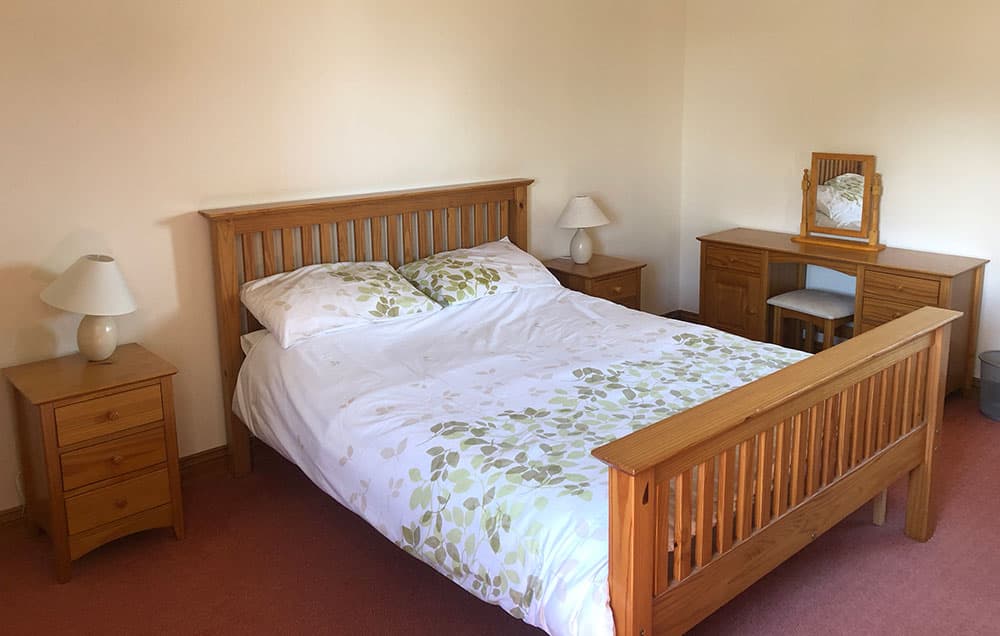 Double bedroom with a pine bed, leaf-patterned bedding, bedside tables with lamps and a dressing table