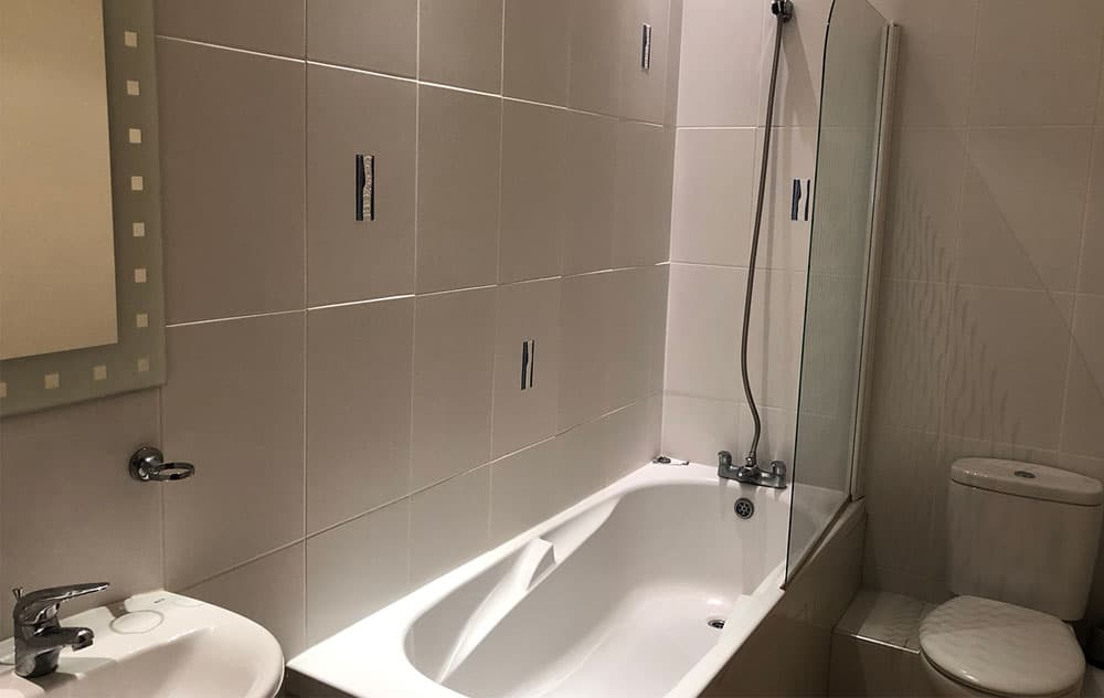 Bathroom with a bath and shower over, basin and toilet, with large grey wall tiles