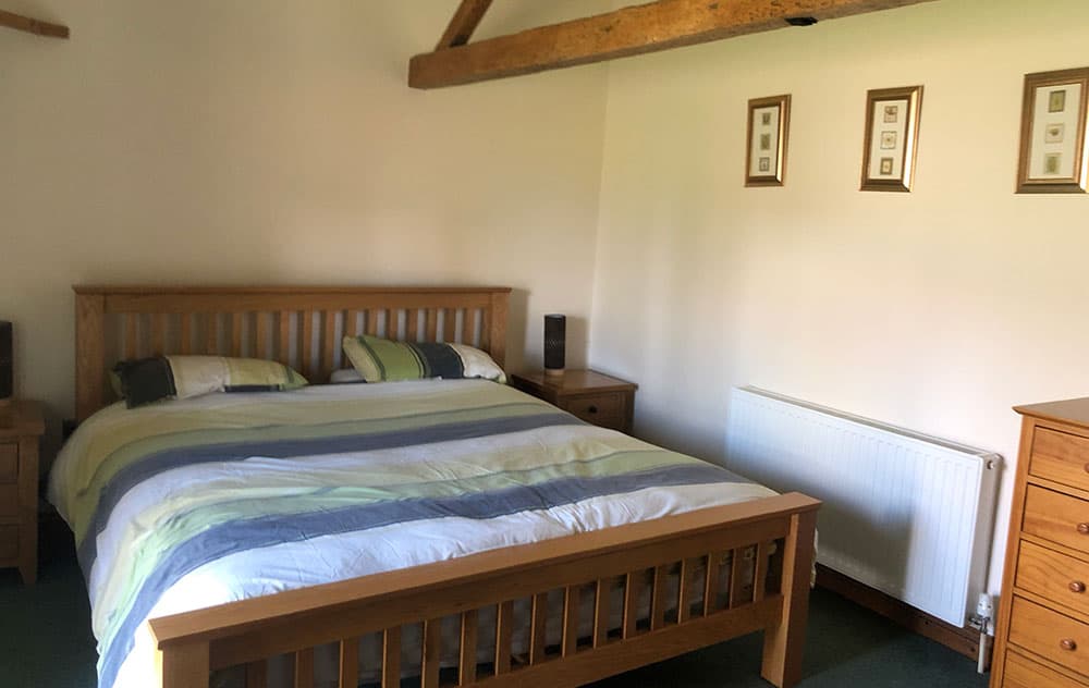 Bedroom with a large pine bed and striped bedding under exposed roof beams
