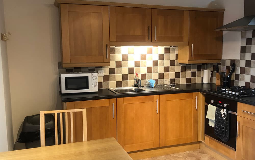 Kitchen with oak units, a microwave, gas hob and oven, and a tiled splashback