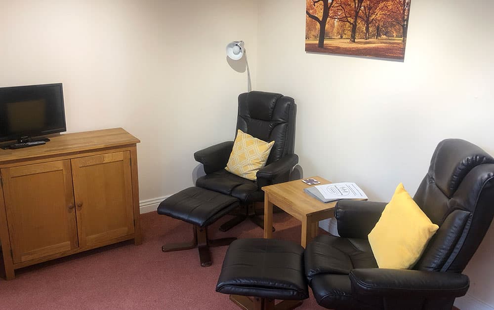 Sitting area with two black leather reclining chairs with footstools, a side table, an oak cupboard and a TV
