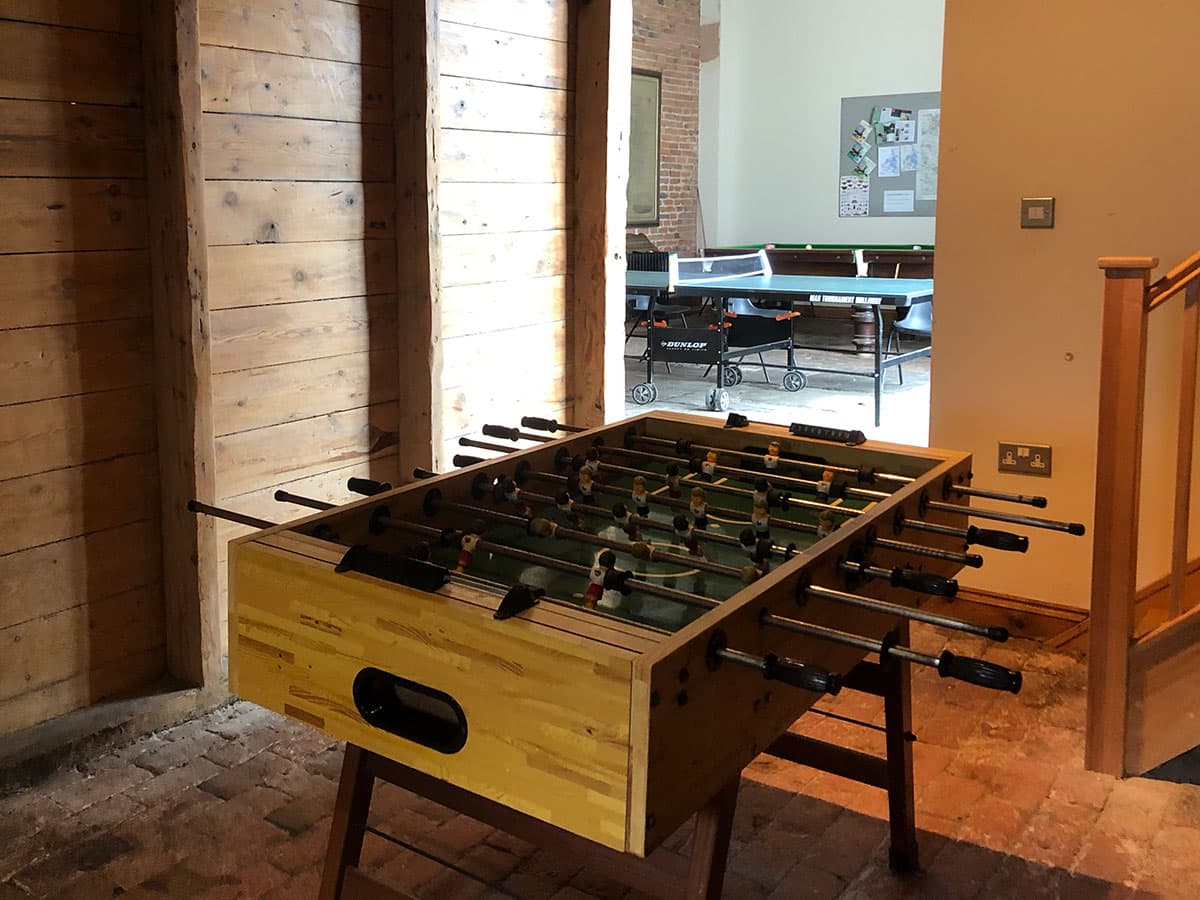 Table football in a timber-clad room, with a table tennis table through the doorway