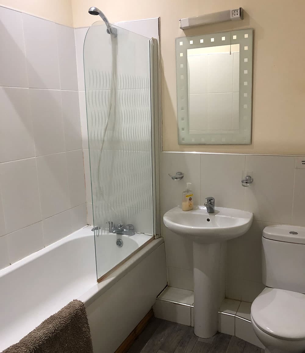 Bathroom with a bath and glass shower screen, pedestal basin, toilet and illuminated mirror