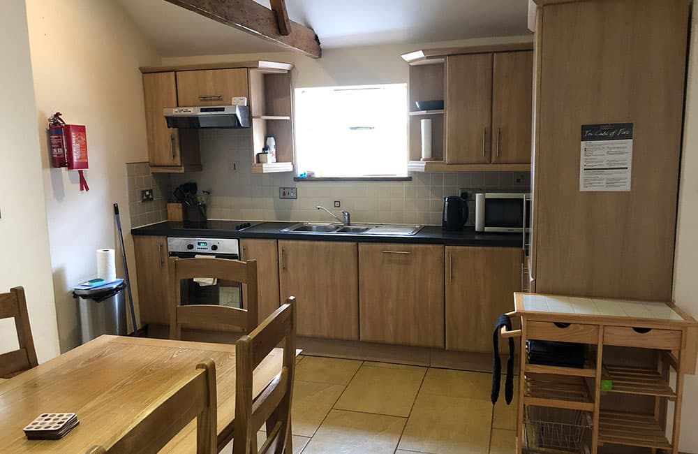 Kitchen with oak units, an oven, a microwave and a trolley, with the dining table in the foreground