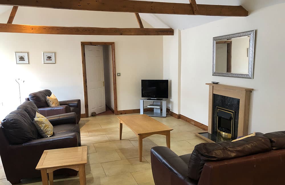 Sitting room with brown leather sofas, a coffee table, a TV and an electric fire under exposed beams