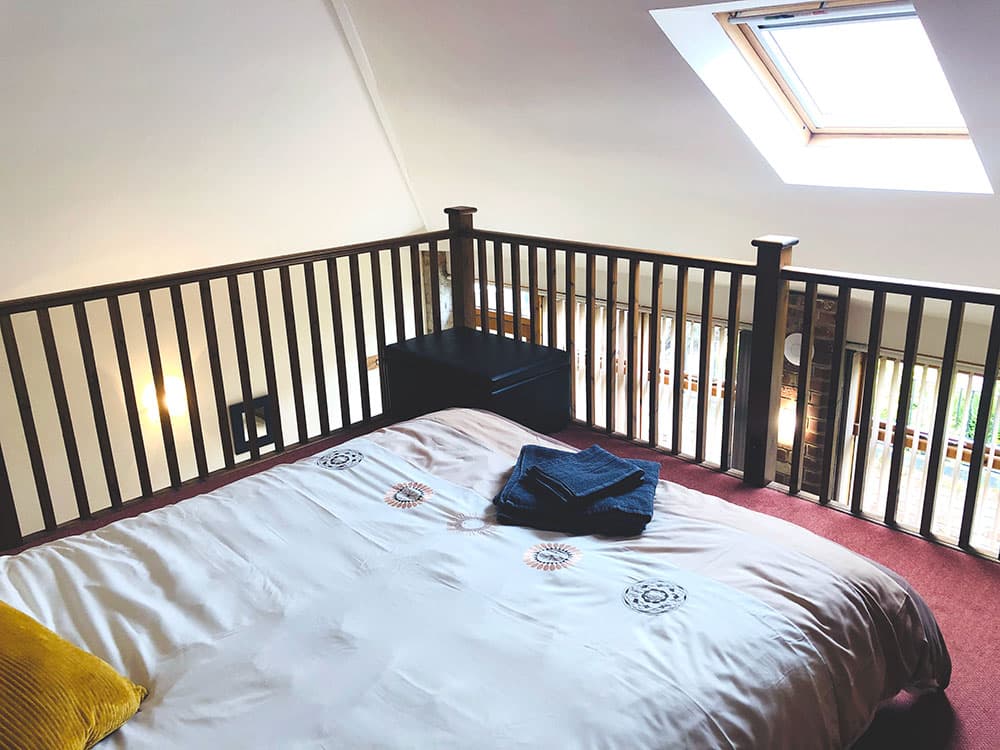 Mezzanine bedroom with a double bed below a skylight and a wooden balustrade overlooking the room below
