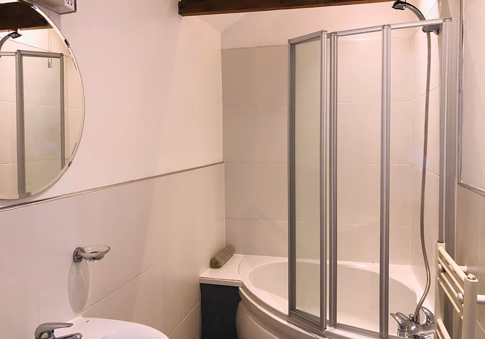 Bathroom with a corner bath, a folding shower screen and a round mirror