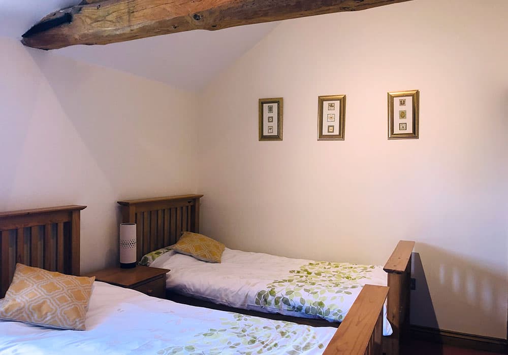 Twin bedroom with two wooden single beds under a beamed ceiling, with three small pictures on the wall