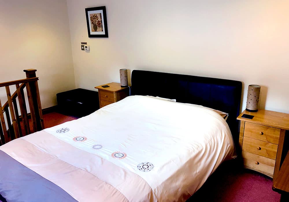 Double bed with a dark headboard and oak bedside cabinets at the top of a staircase