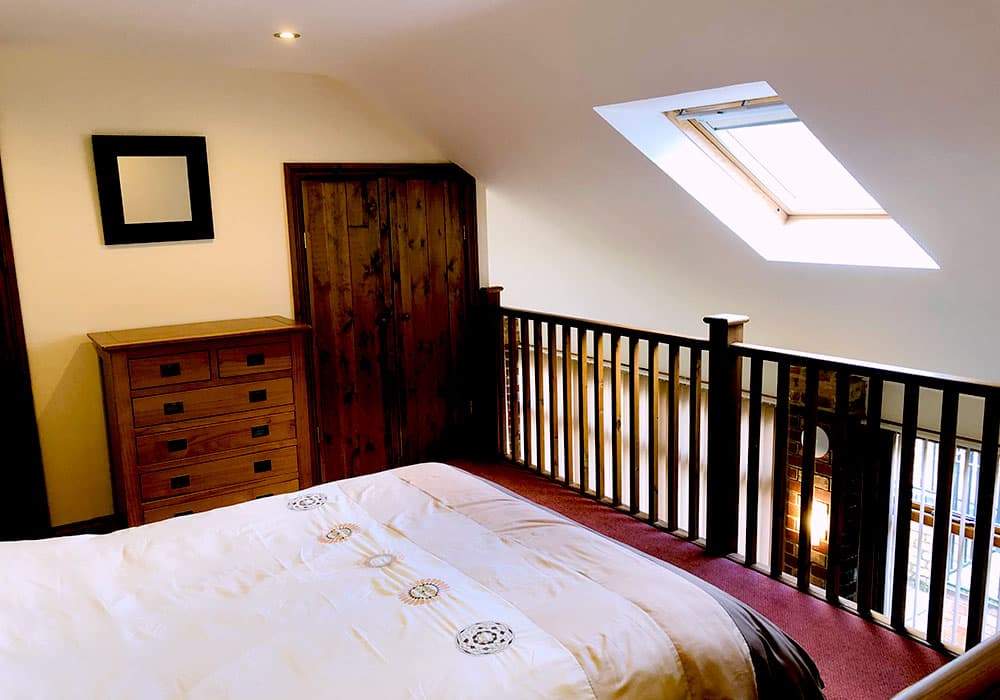 Mezzanine bedroom with a double bed, an oak chest of drawers and a wardrobe under a skylight