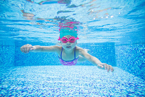 Child in goggles swimming underwater in a blue tiled pool