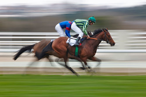 Two racehorses and their jockeys galloping past the rail