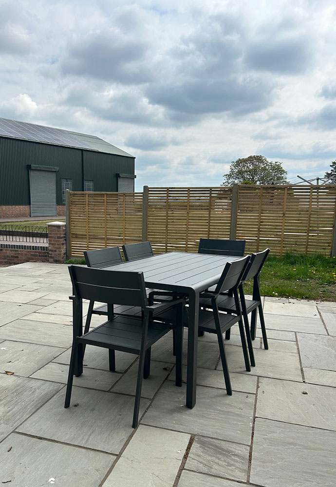 Paved patio with a grey dining table and six chairs, enclosed by a wooden fence